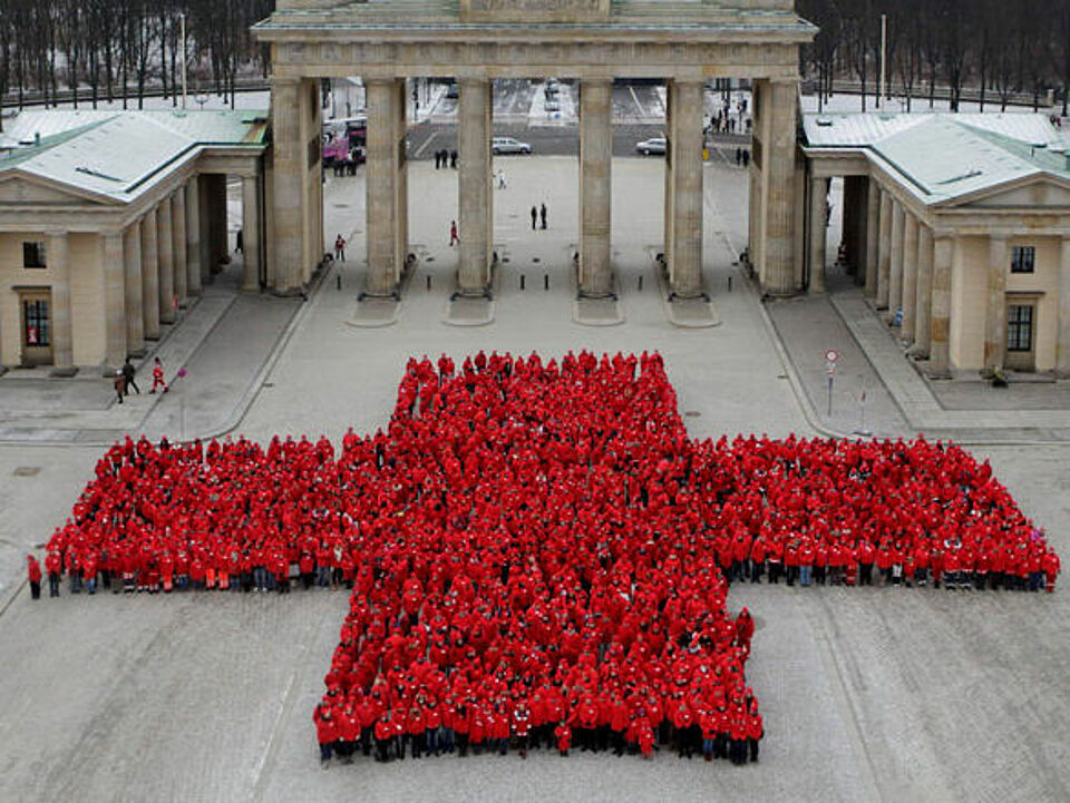Menschen bilden ein großes rotes Kreuz vor dem Brandenburger Tor