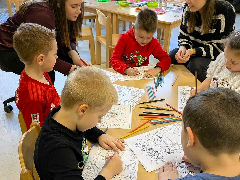 PXL_20251218_085656950.MP Kinder sitzen am Tisch und malen Bilder aus