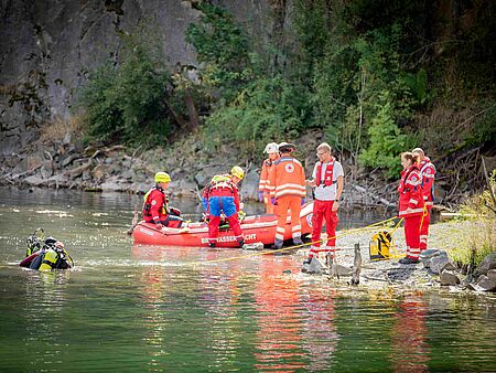 BRK-Retter stehen am Ufer eines Sees, ein Boot hat angelegt ein Taucher ist im Wasser