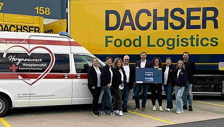 Frauen und Männer stehen mit dem Spendenscheck vor dem Hospizmobil und einem Lkw