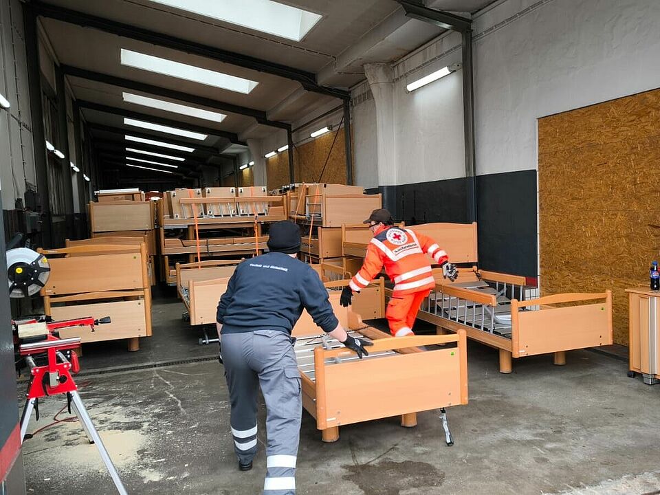 BRK-Helfende schieben ein Bett in die Lagerhalle