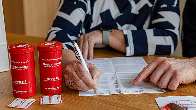 Kundin füllt Patientenbogen der Rotkreuzdose aus