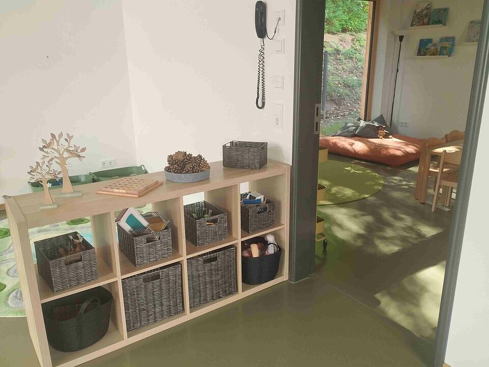 Blick auf ein Regal mit Naturspielsachen und in eine Kissenecke