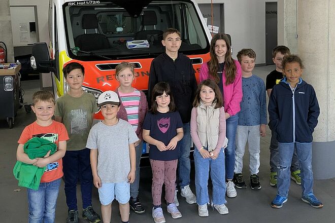 Elf Kinder stehen vor einem Krankentransportwagen