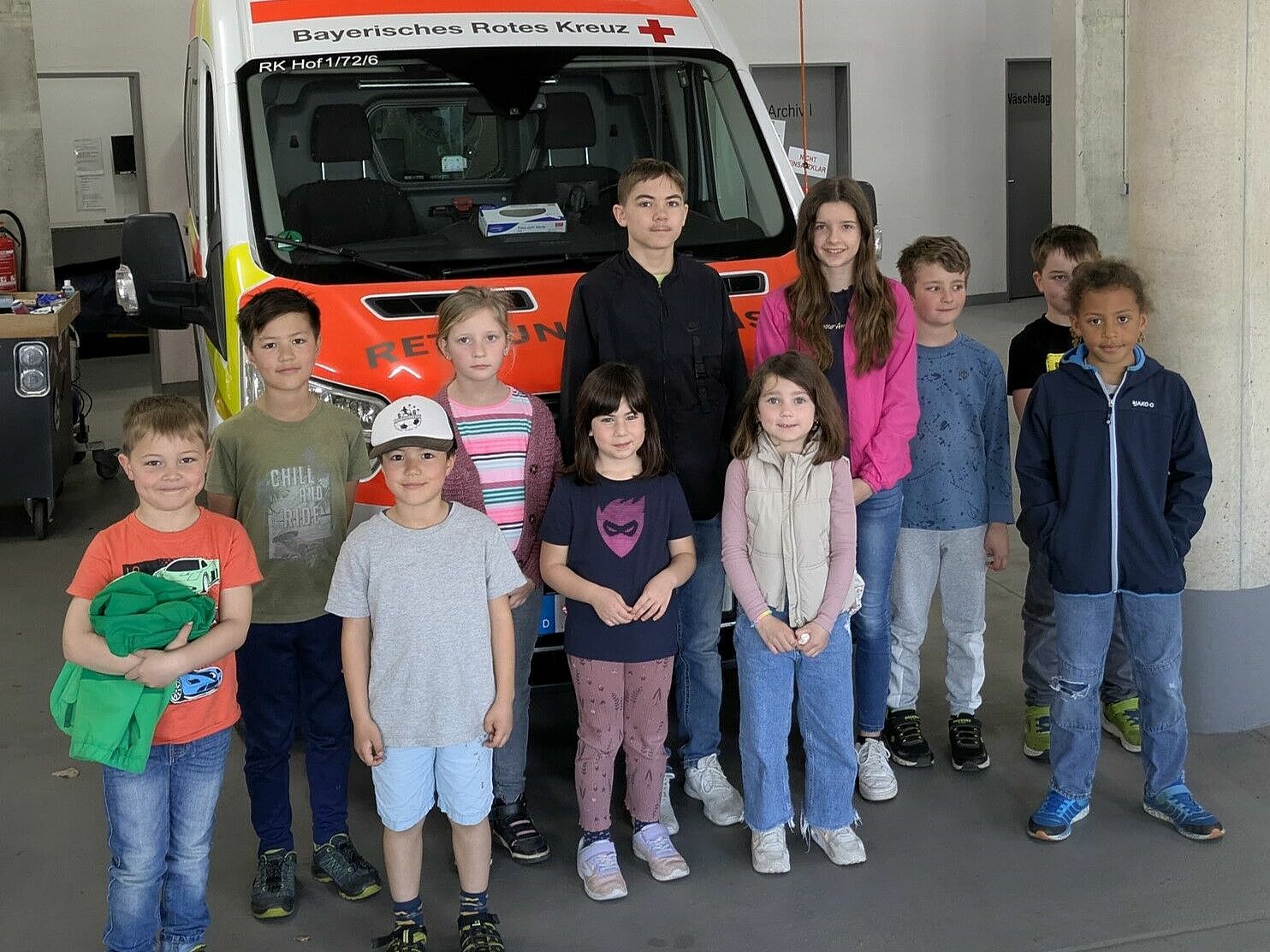 Elf Kinder stehen vor einem Krankentransportwagen
