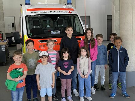 Elf Kinder stehen vor einem Krankentransportwagen