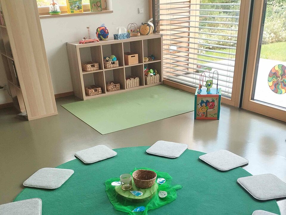 Sitzkissen liegen auf einem teppich, dahinter ein Regal mit Spielsachen