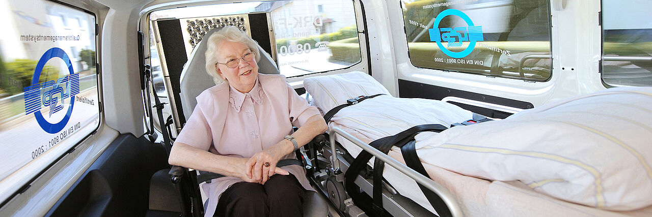 Seniorin sitzt in einem Fahrzeug des Roten Kreuzes