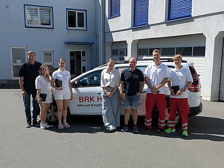 Männer und Frauen stehen in einem Innenhof vor einem Auto