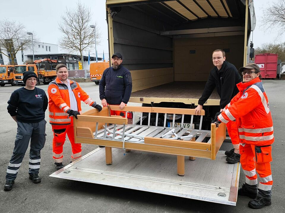 Helfende der Bereitschaft stehen hinter einem offenen LKW
