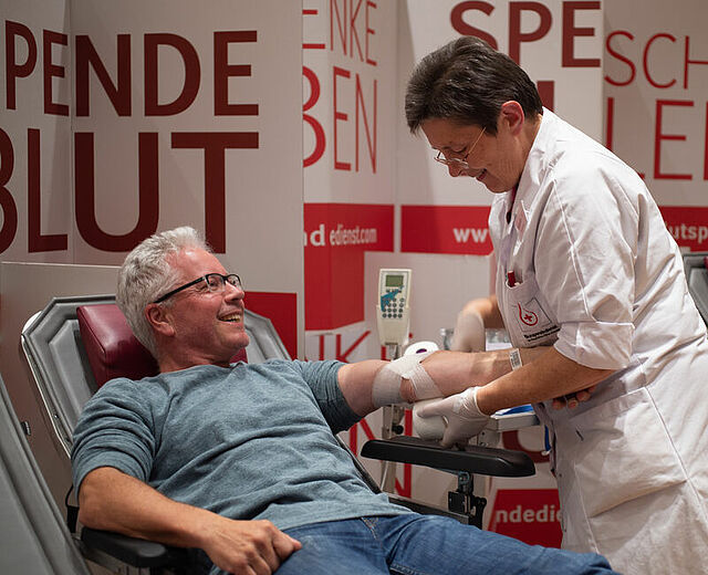 Ein Mann liegt bei der Blutspende auf einer Liege und bekommt einen Verband angelegt