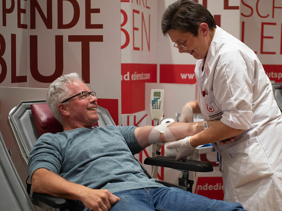 Ein Mann liegt bei der Blutspende auf einer Liege und bekommt einen Verband angelegt