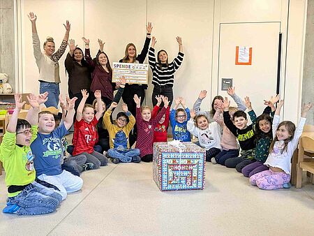 Kinder und Kita-Leitung freuen sich über den Spendenscheck und das Geschenk